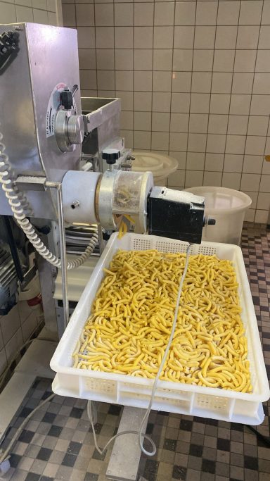 Pasta in einer großen Wanne neben einer Nudelmaschine in einer Küche.