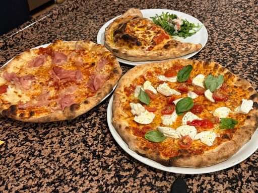 Drei verschiedene Pizzen auf einem Tisch: eine mit Schinken, eine mit Mozzarella und Basilikum.