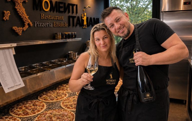 Alina & Luca Ein Paar in schwarzen Schürzen hält ein Glas und eine Flasche Sekt in einem italienischen Restaurant.